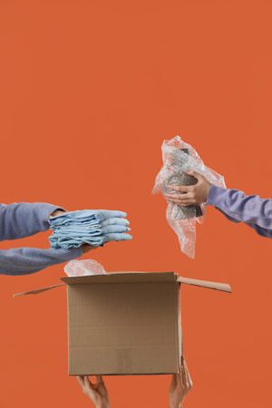 Women packing things in moving box on orange background
