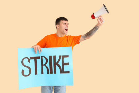 Protesting young man holding placard with the word STRIKE and megaphone on beige backgroundの写真素材