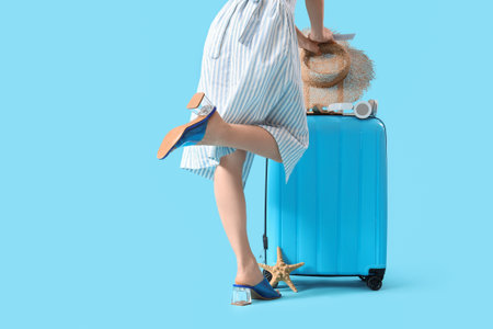 Female traveler with suitcase and beach accessories on blue backgroundの写真素材