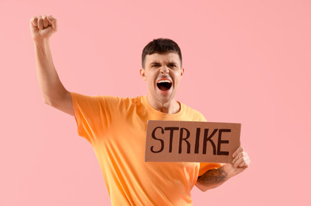 Protesting young man holding placard with the word STRIKE against pink backgroundの写真素材