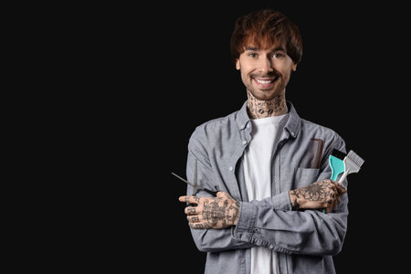 Young tattooed barber with brushes and scissors on dark backgroundの写真素材