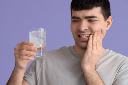 Young man with cool water suffering from toothache on lilac background, closeupの写真素材