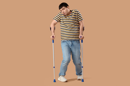 Young man with crutches on brown background. National Cerebral Palsy Awareness Monthの写真素材