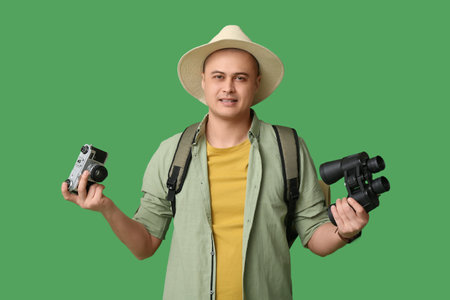 Young male tourist with backpack, photo camera and binoculars on green backgroundの写真素材