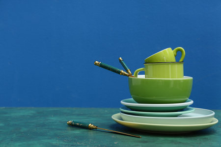 Stack of green clean tableware and cutlery on table against blue backgroundの写真素材