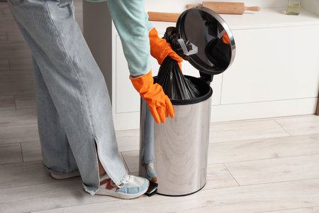 Woman taking full garbage bag from trash bin in light kitchenの写真素材