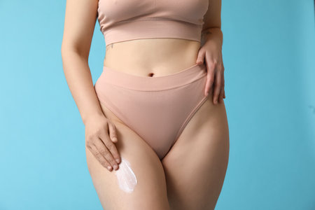 Beautiful young woman with anti-cellulite cream on blue background, closeupの写真素材
