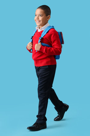 Happy little African-American schoolboy with backpack on blue backgroundの写真素材