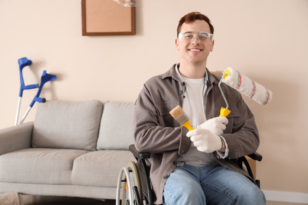 Young man in wheelchair with paint roller and brush during repair at homeの写真素材