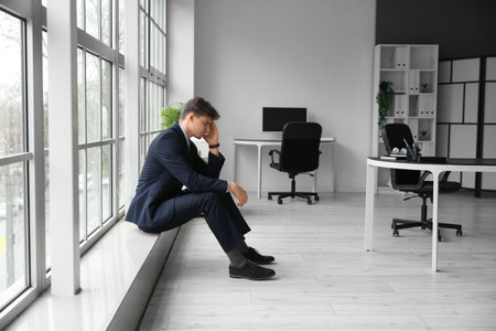 Young businessman suffering from headache near window in officeの写真素材