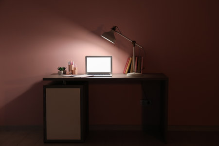 Table with modern laptop and glowing lamp near pink wallの写真素材