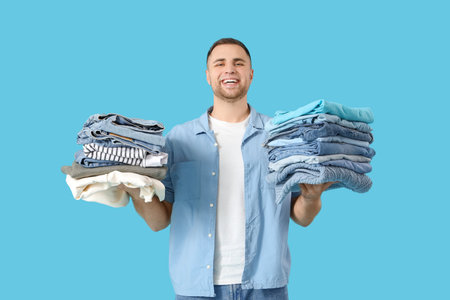 Young man with stacks of clothes on blue background