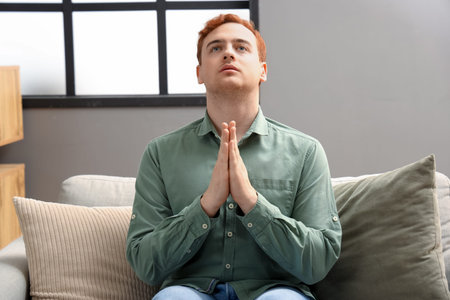 Young man praying on sofa at home