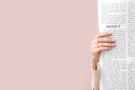 Female hand with newspaper on pink background, closeupの写真素材