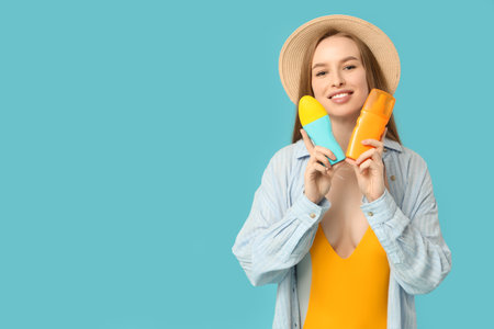 Beautiful young happy woman with bottles of sunscreen cream on blue background