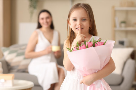 Cute little girl with tulips for her mother showing silence gesture at homeの写真素材