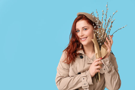 Happy young woman with pussy willow branches on blue background. Easter celebration