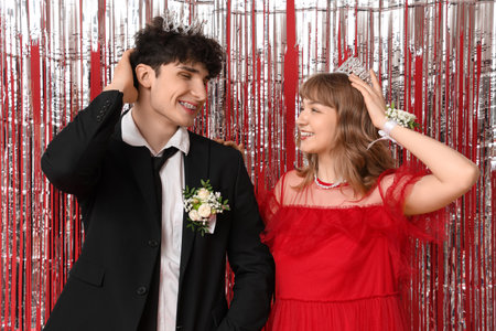 Happy prom couple in crowns with tinsel on red backgroundの写真素材