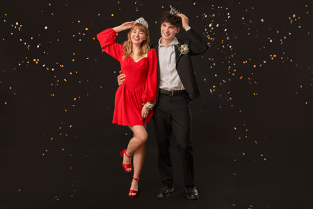 Happy prom couple with crowns and confetti on black backgroundの写真素材