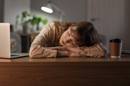 Young woman sleeping on table near laptop in office