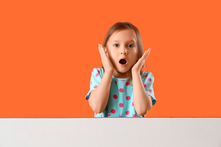 Shocked little girl with blank poster on orange backgroundの写真素材