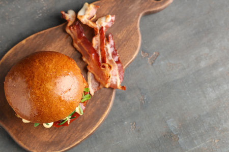 Wooden board with tasty burger and bacon on gray grunge backgroundの写真素材