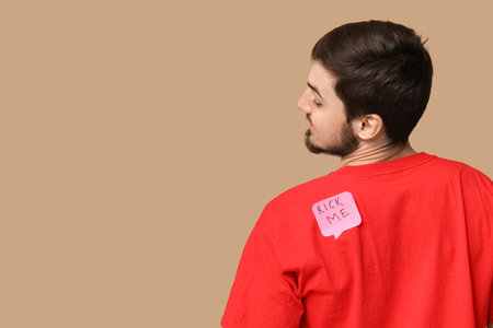 Handsome young man with sticker attached to his back on brown background. April fool's day celebrationの写真素材