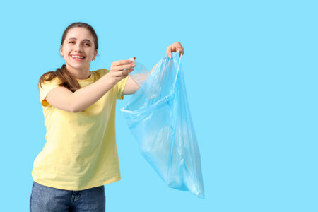 Young woman throwing plastic bottle into garbage bag on blue background. Waste sorting conceptの写真素材