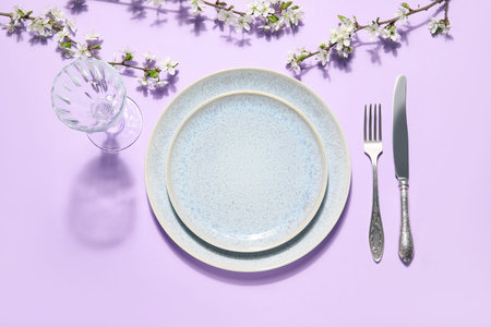 Beautiful table setting with blossoming branches on lilac background