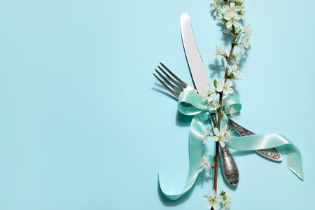 Silver cutlery with blossoming branch on blue backgroundの写真素材