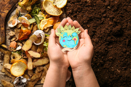 Female hands holding happy paper Earth sign near organic waste and soil, closeup. Compost recycling...