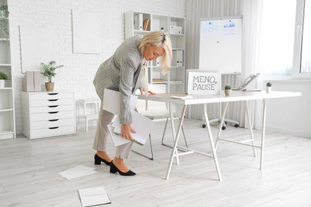 Mature businesswoman dropping papers in office. Menopause concept