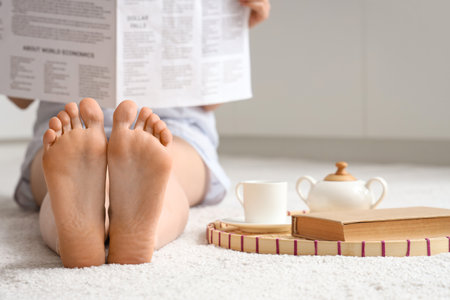 Barefoot woman with newspaper sitting on white carpet in kitchen, closeupの写真素材