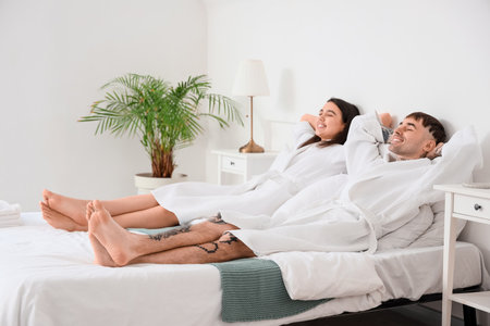 Couple of tourists lying on bed in hotel roomの写真素材