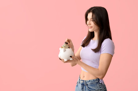 Beautiful young happy woman with piggy bank and money on pink backgroundの写真素材