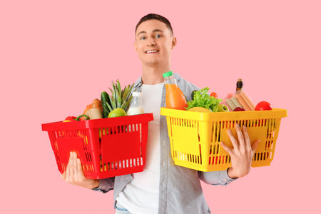 Young man with full shopping baskets on pink backgroundの写真素材
