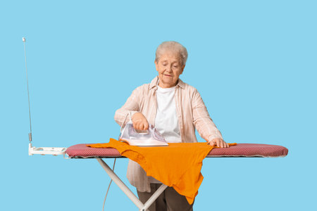 Senior woman with ironing t-shirt on blue backgroundの写真素材
