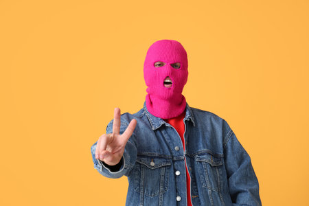 Handsome young man in balaclava showing victory gesture on yellow backgroundの写真素材