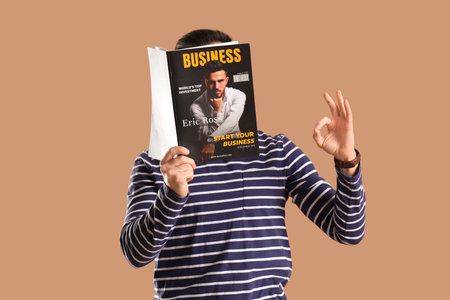 Young man with magazine showing OK on brown backgroundの写真素材