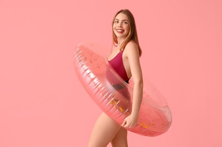 Beautiful young woman in tank swimsuit and with inflatable ring on pink backgroundの写真素材