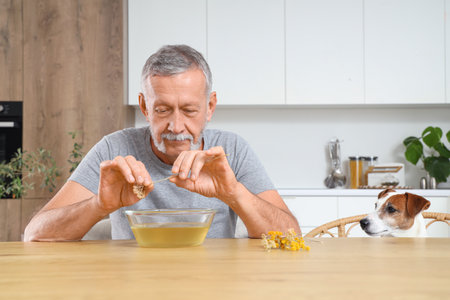 Mature man with dog preparing steam inhalation at table in kitchenの写真素材