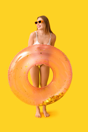 Pretty young woman in tank swimsuit and with inflatable ring on yellow backgroundの写真素材