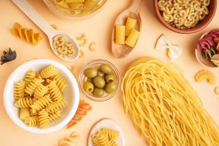 Bowls with different uncooked pasta and olives on beige backgroundの写真素材