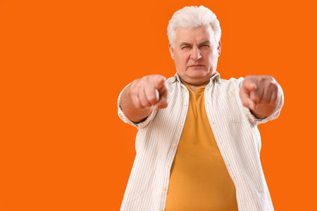 Mature man pointing at viewer on orange background. Accusation conceptの写真素材