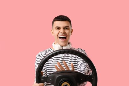 Emotional young man with steering wheel and headphones on pink backgroundの写真素材
