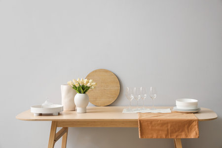 Clean tableware and tulip flowers on wooden table near light wallの写真素材