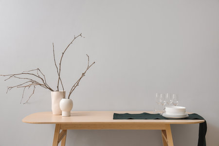 Clean tableware and vases with tree branches on wooden table near light wallの写真素材