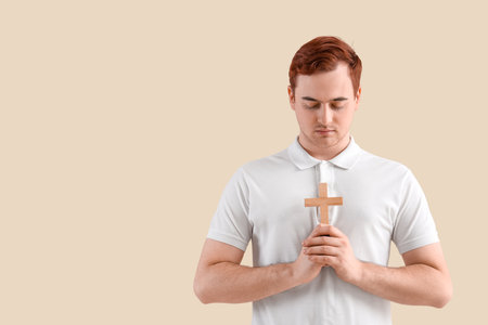 Young man with cross praying on beige backgroundの写真素材