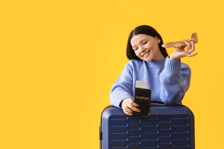 Beautiful young woman with wooden plane, passport and suitcase on yellow backgroundの写真素材