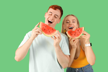 Young beautiful man and woman with slices of fresh watermelon on green backgroundの写真素材